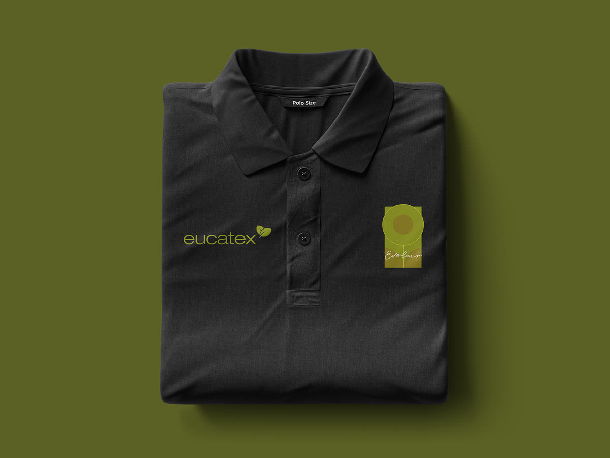 Camisa polo preta dobrada e vista de cima sobre fundo verde-oliva, com o logotipo eucatex e o selo Evoluir.