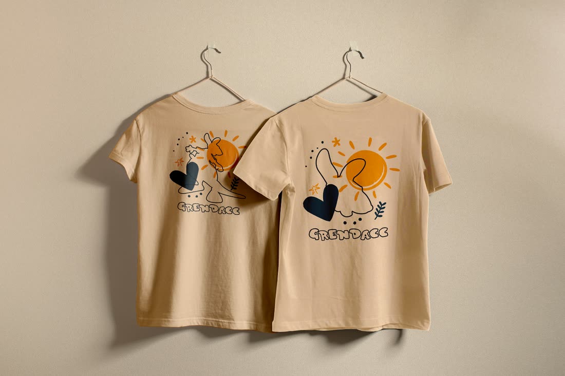 Duas camisetas bege do Grendacc com ilustrações coloridas, em cabides.