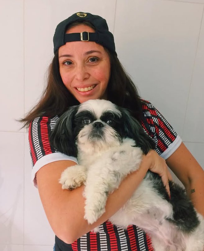 A mãe de Gianluca, de boné, com o cachorro no colo e vestindo a camisa do Paulista com as listras desenhadas a partir dos trilhos.